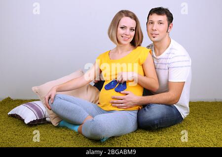 Jeune femme enceinte tenant des chaussettes de bébé avec son mari sur le sol à la maison Banque D'Images