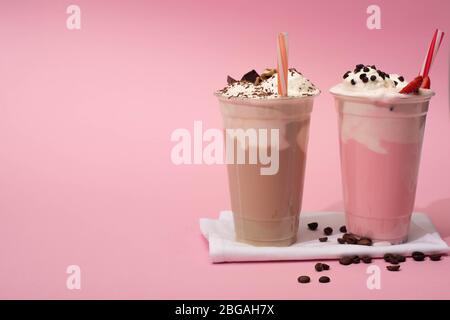 Tasses jetables de milkshakes au chocolat et aux fraises avec pailles à boire et grains de café sur serviettes de table roses Banque D'Images