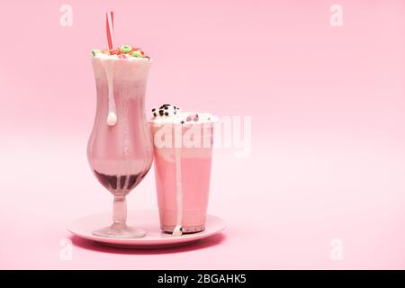 Tasse jetable et verre de milk-shakes aux fraises sur plaque sur fond rose Banque D'Images