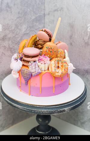 Gâteau d'anniversaire rose et orange décoré de macarons, meringues, beignets, gaufres, gâteaux et barres de chocolat. Banque D'Images