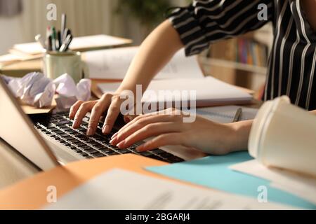 Gros plan sur les mains désorganisées de l'entrepreneur travaillant sur un ordinateur portable sur un bureau désorganisé la nuit au bureau à domicile Banque D'Images