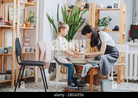 Femme et garçon façonnant un bol en argile sur une roue de poterie dans un atelier privé Banque D'Images