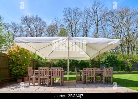 Parasol sur un mobilier de jardin en bois sur un patio dans un jardin, le printemps ensoleillé. Banque D'Images