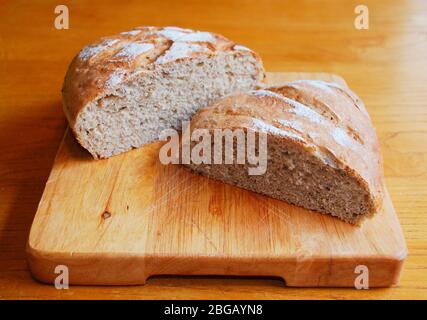 Deux pains de pain maison au levain sur une planche à découper en bois sur une table en bois dans un éclairage naturel Banque D'Images