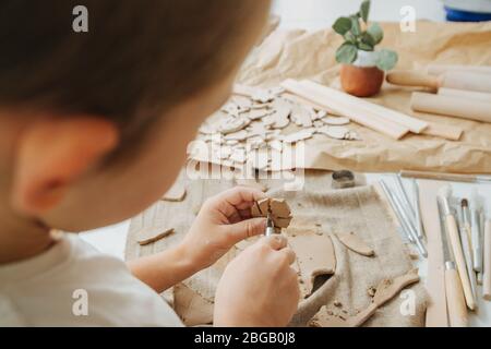 Petit garçon travaillant avec de l'argile dans un atelier, le coupant en forme de feuille Banque D'Images