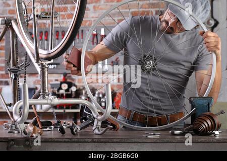 l'homme répare la bicyclette vintage dans l'atelier de garage sur l'établi avec des outils, enlever la rouille avec du papier de sable, concept de bricolage Banque D'Images