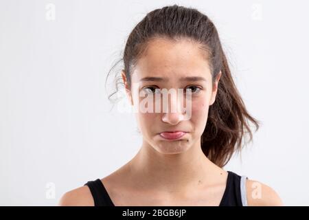 Sulky misérable jeune femme poulant ses lèvres et regardant l'appareil photo avec des yeux affligeant dans une tête de gros plan tourné sur blanc Banque D'Images