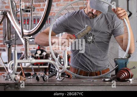 l'homme répare la bicyclette vintage dans l'atelier de garage sur l'établi avec des outils, concept de bricolage Banque D'Images