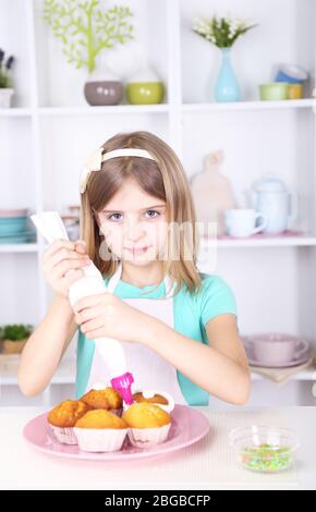 Petite fille décorant des cupcakes dans la cuisine à la maison Banque D'Images