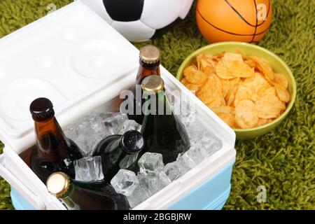 Glacière pleine de boissons dans des bouteilles sur fond de tapis couleur Banque D'Images
