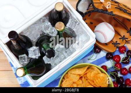 Glacière pleine de boissons dans des bouteilles sur une serviette de couleur, sur fond en bois Banque D'Images