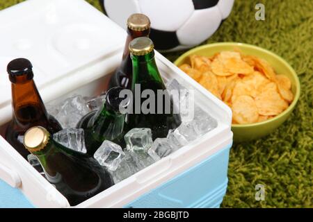 Glacière pleine de boissons dans des bouteilles sur fond de tapis couleur Banque D'Images
