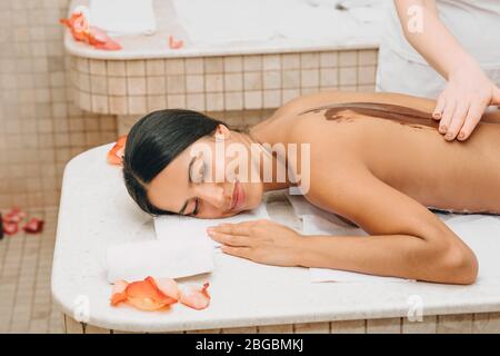 Femme mixte recevant un masque au chocolat au salon de spa. La procédure de masque corporel au chocolat nourrit la peau de vitamines, de minéraux et d'antidépre Banque D'Images