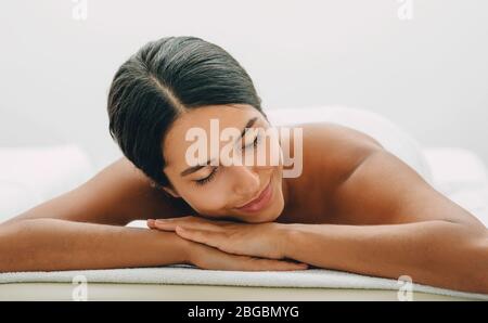 Une femme de course mixte se détend sur une table de massage après s'être relaxante au spa et au massage. Banque D'Images