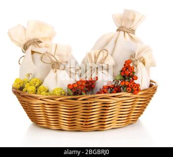 Sachets de textiles avec fleurs séchées, herbes et baies dans un panier en osier, isolés sur blanc Banque D'Images