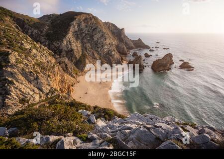 Plage de Praia da Ursa au coucher du soleil, située à Sintra, Portugal. Paysage scène de plage de sable, rochers de la pile de mer et vagues de l'océan illuminées par la lumière dorée. Surre Banque D'Images