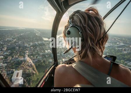 Portrait de belles femmes blondes en hélicoptère. Elle est stupéfiée par la ville et porte des écouteurs pilotes. Banque D'Images