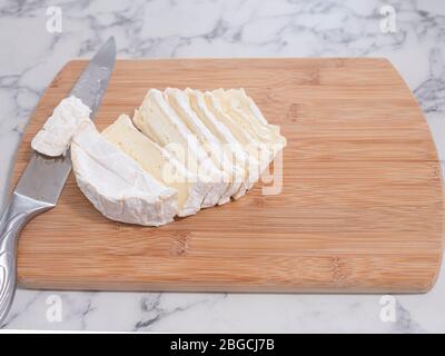 Fromage Brie frais, tranché, avec un couteau sur un plan de découpe en bois, surface, comptoir en marbre. Banque D'Images