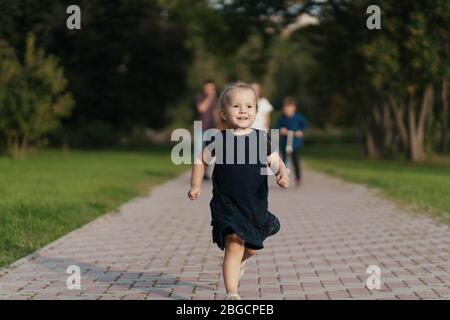 Jolie petite fille qui courir heureuse alors que sa mère, son frère, son père la suit tout en marchant dans le parc Banque D'Images