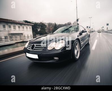 Berline noire avec feux avant blancs sur l'autoroute dans les villes en hiver Banque D'Images