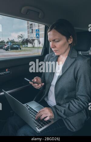 Businesswoman using mobile phone and laptop computer in car ensemble assis à la banquette arrière, la communication d'entreprise à l'étranger Banque D'Images