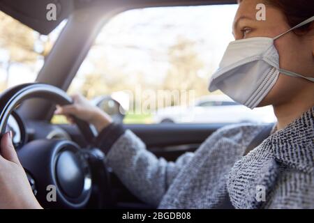 Jeune femme conducteur portant un masque de protection conduisant la voiture au travail. Banque D'Images