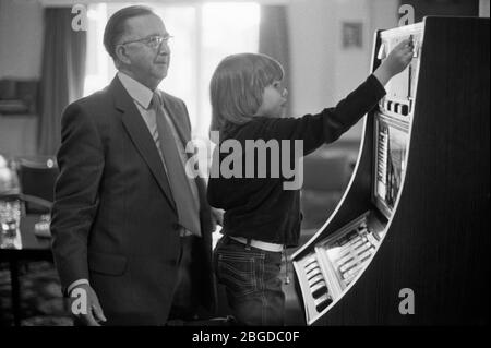 Enfant jouant une machine à fruits, jeu de hasard de chance, en essayant de gagner 1981 grand-père regardant les années 1980 Didsbury, Manchester, Angleterre Royaume-Uni des années 1980 HOMER SYKES Banque D'Images