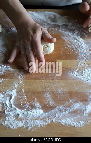 Concept de cuisine maison. Mains féminines préparant de petites boules de pâte à pizza maison fraîche sur planche en bois farinée. Gros plan. Cuisine italienne. Banque D'Images