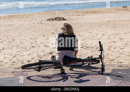 Poole, Dorset Royaume-Uni. 21 avril 2020. Temps au Royaume-Uni : belle journée chaude et ensoleillée, les températures montent sur les plages de Poole sur la côte sud, les gens prennent leur exercice autorisé, en respectant la plupart des directives du coronavirus. Femme assise sur la promenade avec un bicle. Crédit : Carolyn Jenkins/Alay Live News Banque D'Images