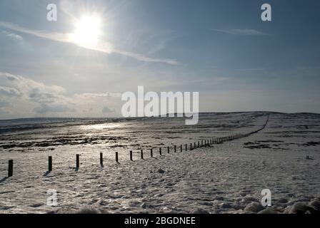 Des landes couvertes de neige solitaire avec un soleil bas reflétant la neige et mettant en évidence une barrière qui traverse l'horizon lointain Banque D'Images