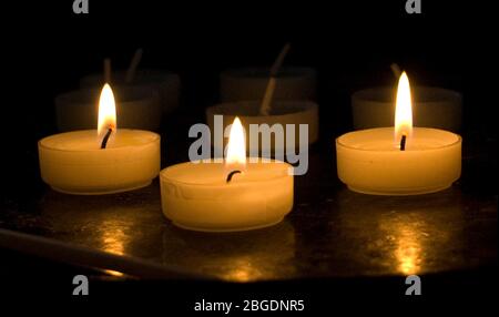 Vue rapprochée de trois bougies votives allumées sur un stand avec d'autres sans lumière derrière et fondu en arrière-plan
