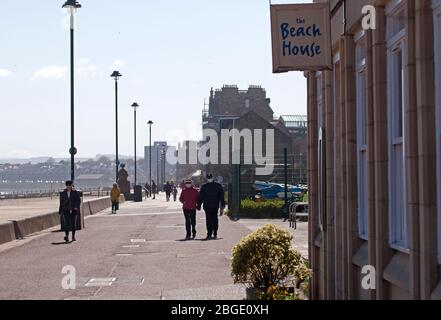 Portobello, Édimbourg, Écosse, Royaume-Uni. 21 avril 2020. Comme l'éclusage de Coronavirus continue le public qui sont dehors avant midi profiter du soleil au bord de la mer, cependant, photo un couple âgé portant des masques de protection. Un vent frais de 30 km/h avec des rafales potentielles de 46 km/h n'encourage pas ceux qui sont dehors à s'asseoir pendant très longtemps. Trois endroits sont maintenant ouverts pour la nourriture à emporter, Muro's Bistro, la Beach House et le pub Espy a retiré les volets de leurs fenêtres. Crédit: Arch White/ Alay Live News. Banque D'Images