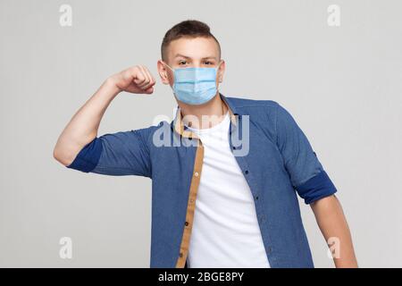 Je suis fort. Portrait de jeune homme haughty dans un style décontracté avec masque médical chirurgical debout avec bras levés et regardant l'appareil photo avec un visage fier. Banque D'Images