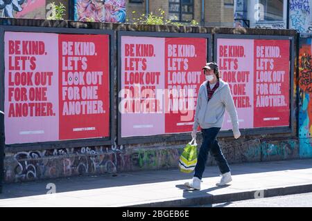 Un homme portant un masque de protection passe devant une rangée d'affiches à Shoreditch, dans l'est de Londres, alors que le Royaume-Uni continue à se maintenir en place pour aider à freiner la propagation du coronavirus. Banque D'Images