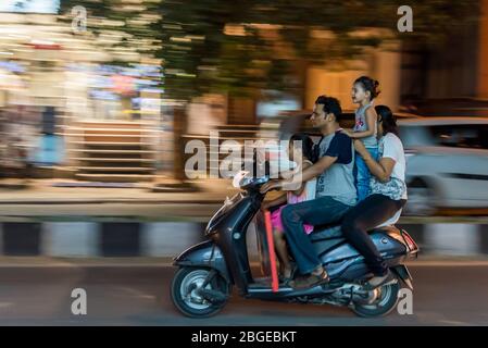 Flou de mouvement granuleux prise d'une famille de quatre personnes qui se déplace sur un scooter sans porter de casque dangereusement Banque D'Images