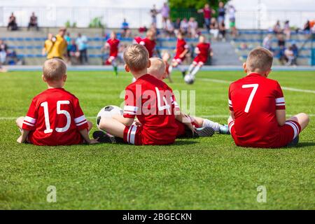 Équipe de sport pour enfants de niveau junior assise sur le terrain de gazon. Football Football enfants joueurs debout ensemble pendant le jeu de compétition de football d'école. Garçons i Banque D'Images