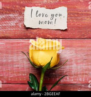 Une rose jaune et un morceau de papier avec le texte je t'aime maman écrit en C, sur une surface en bois rustique rouge Banque D'Images