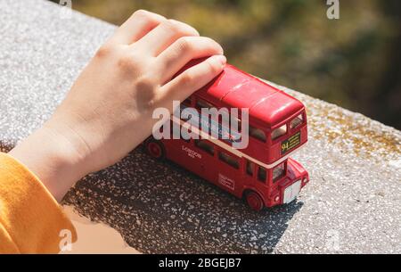 Main de petit enfant jouant avec un jouet de bus rouge à impériale Banque D'Images