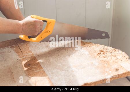 Main de travail féminine sciant une planche en bois dans un atelier. Concept de réparation à domicile Banque D'Images