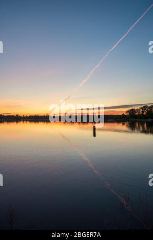 Magnifique coucher de soleil sur le lac Kralingse Plas à Rotterdam. La trace de condensation d'un avion est rose par la lumière du soleil couchant. Banque D'Images