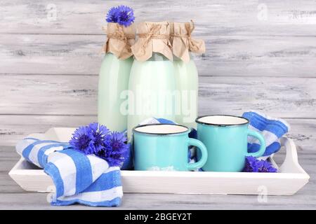 Bouteilles et tasses de lait avec des fleurs de maïs sur plateau en bois Banque D'Images