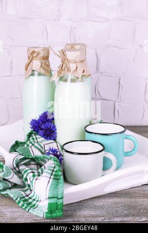 Bouteilles et tasses de lait avec des fleurs de maïs sur plateau en bois Banque D'Images