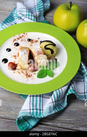 Délicieux strudel aux pommes maison avec noix, feuilles de menthe et glace sur plaque, sur fond de bois Banque D'Images