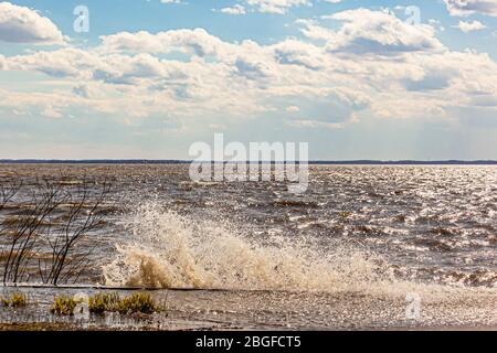 Vagues du lac éclaboussant sur un mur de mer, par une journée ensoleillée et venteuse avec des nuages cumulés. Banque D'Images