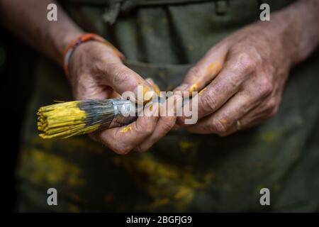 Gros plan des mains de peintre senior tenant un pinceau de peinture jaune. Banque D'Images
