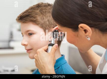 médecin examinant l'oreille de garçon, en utilisant l'otoscope, dans le bureau de médecins. Enfant soumis à un test auditif Banque D'Images