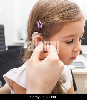 La main coupée de médecin introduit un appareil auditif dans l'oreille de l'enfant Banque D'Images