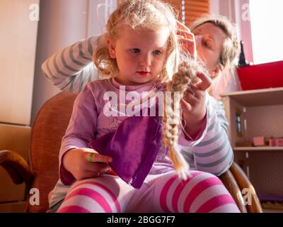 Une fille de deux ans (presque trois) est vérifiée pour les poux de tête par sa mère. Elle tient une poupée de Rainnzel Banque D'Images