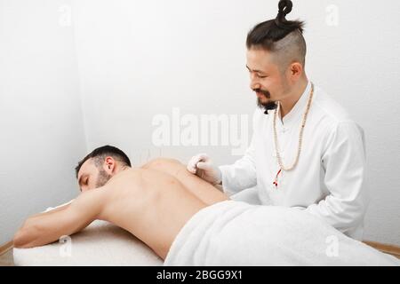 Réflexologue faisant de l'acupuncture pour traiter le patient masculin. L’acupuncture fait partie de la médecine chinoise traditionnelle Banque D'Images