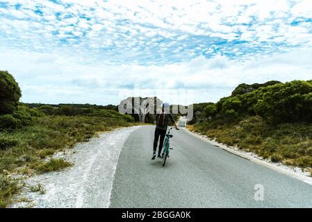 Homme touristique à vélo sur l'île de Rottnest, Australie occidentale. En vélo sur une route sinueuse bordée d'arbustes verts Banque D'Images